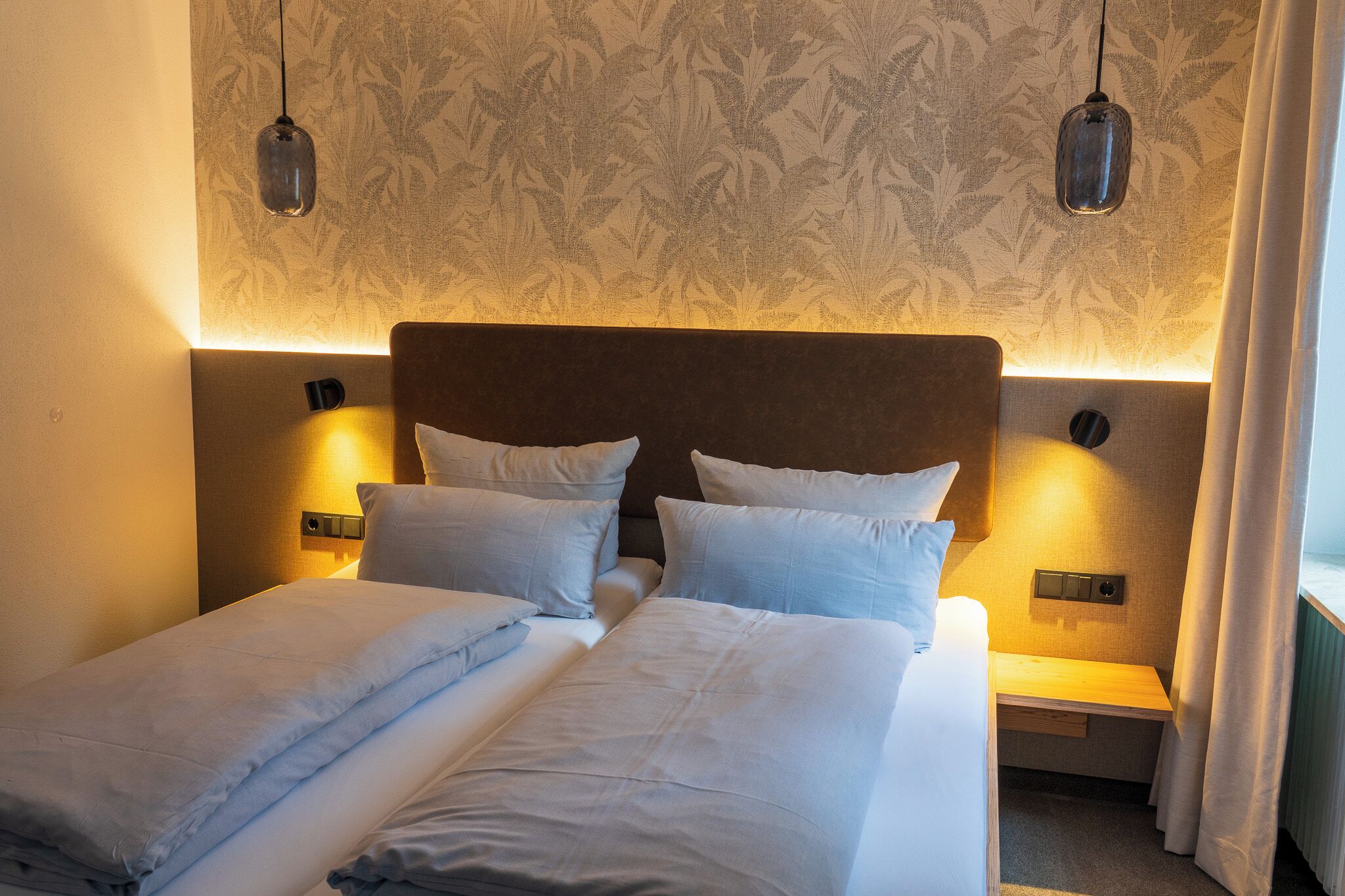 Cama doble con sábanas blancas, cabecera, mesitas de noche y lámparas de pared.