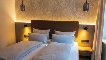 A double bed with white linens, a headboard, bedside tables, and wall-mounted lamps.