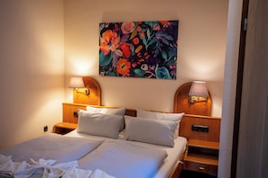 Une chambre d’hôtel avec un lit, deux lampes de chevet, une table de chevet, une tête de lit en bois et un tableau floral accroché au mur.