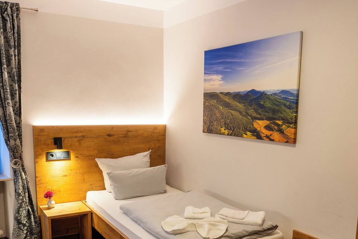 A neatly made bed with pillows, a bedside table with a lamp, and a painting on the wall.