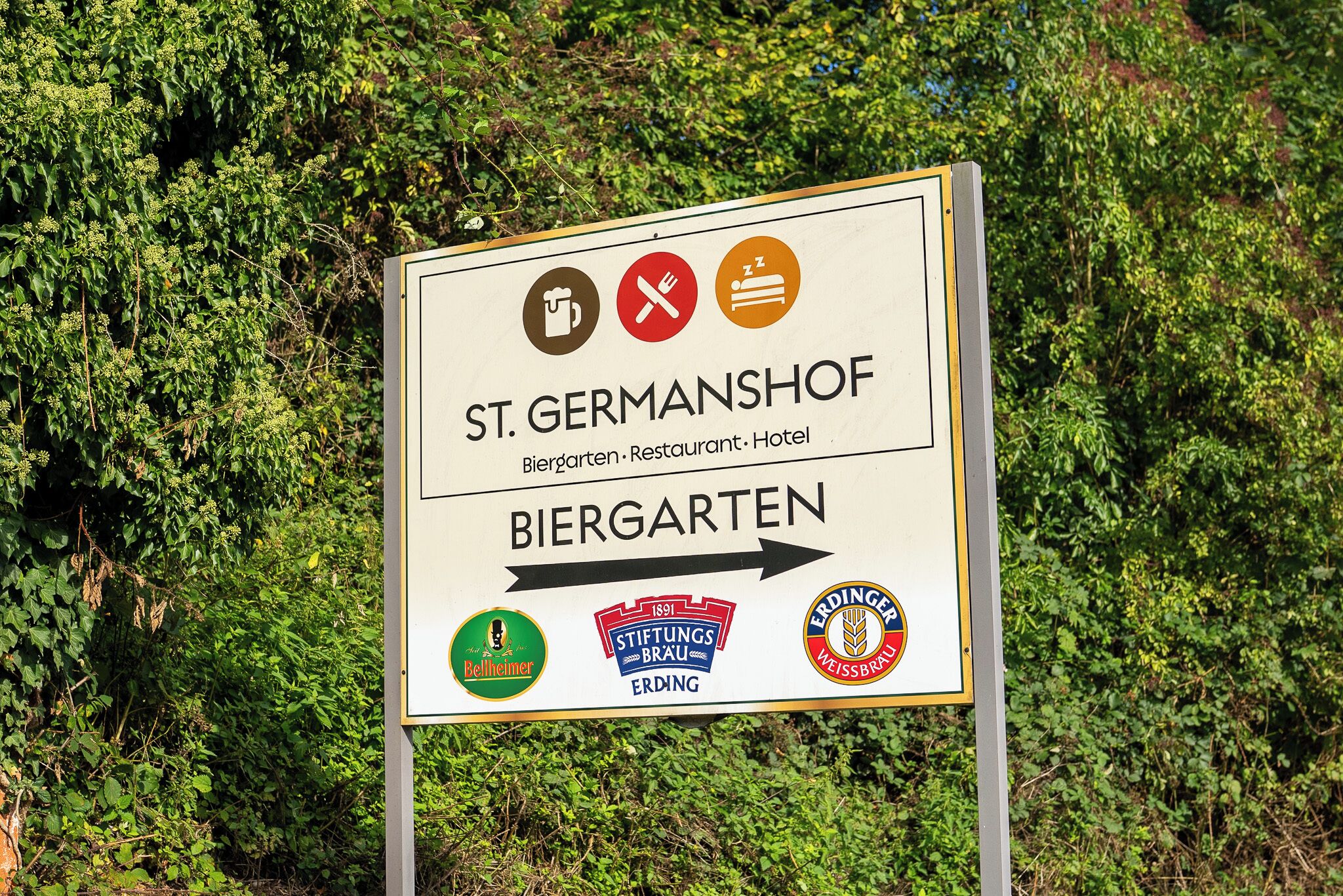 Un panneau indiquant l’emplacement de St. Germanshof, un hôtel-restaurant, avec des flèches directionnelles et les logos de Bellheimer, Stiftungsbrau et Erdinger Weissbrau.