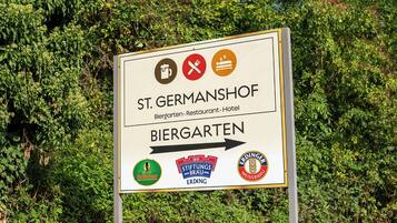 Un panneau indiquant l’emplacement de St. Germanshof, un hôtel-restaurant, avec des flèches directionnelles et les logos de Bellheimer, Stiftungsbrau et Erdinger Weissbrau.
