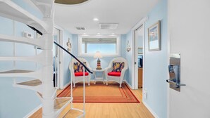 Ein modernes Interieur mit einer Wendeltreppe, zwei Stühlen mit roten Kissen, einem kleinen Tisch mit einer Lampe und Blick durch ein Fenster.