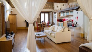 A cozy living room with a wooden floor, a white sofa, a wooden coffee table, and a dining area with a red chair. - Suite Apartment Voltumna (Orvieto)