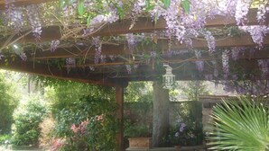 A wooden pergola with hanging purple flowers, a lantern, and a stone bench. - Suite Apartment Voltumna (Orvieto)
