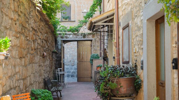 A narrow courtyard with stone walls, a wooden door, and outdoor seating. - Suite Apartment Voltumna (Orvieto)