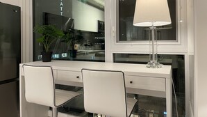 Une chambre d’hôtel moderne avec un bureau blanc, deux chaises, une lampe et une plante en pot.