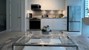 Une cuisine moderne avec des meubles blancs, des appareils en acier inoxydable et une table basse en verre.