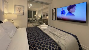Une chambre d’hôtel équipée d’un lit, d’une télévision, d’un bureau et d’une salle de bain visible à travers une porte en verre.