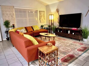 Un salón con un sofá modular, un televisor, una mesa de centro de madera y una alfombra estampada.
