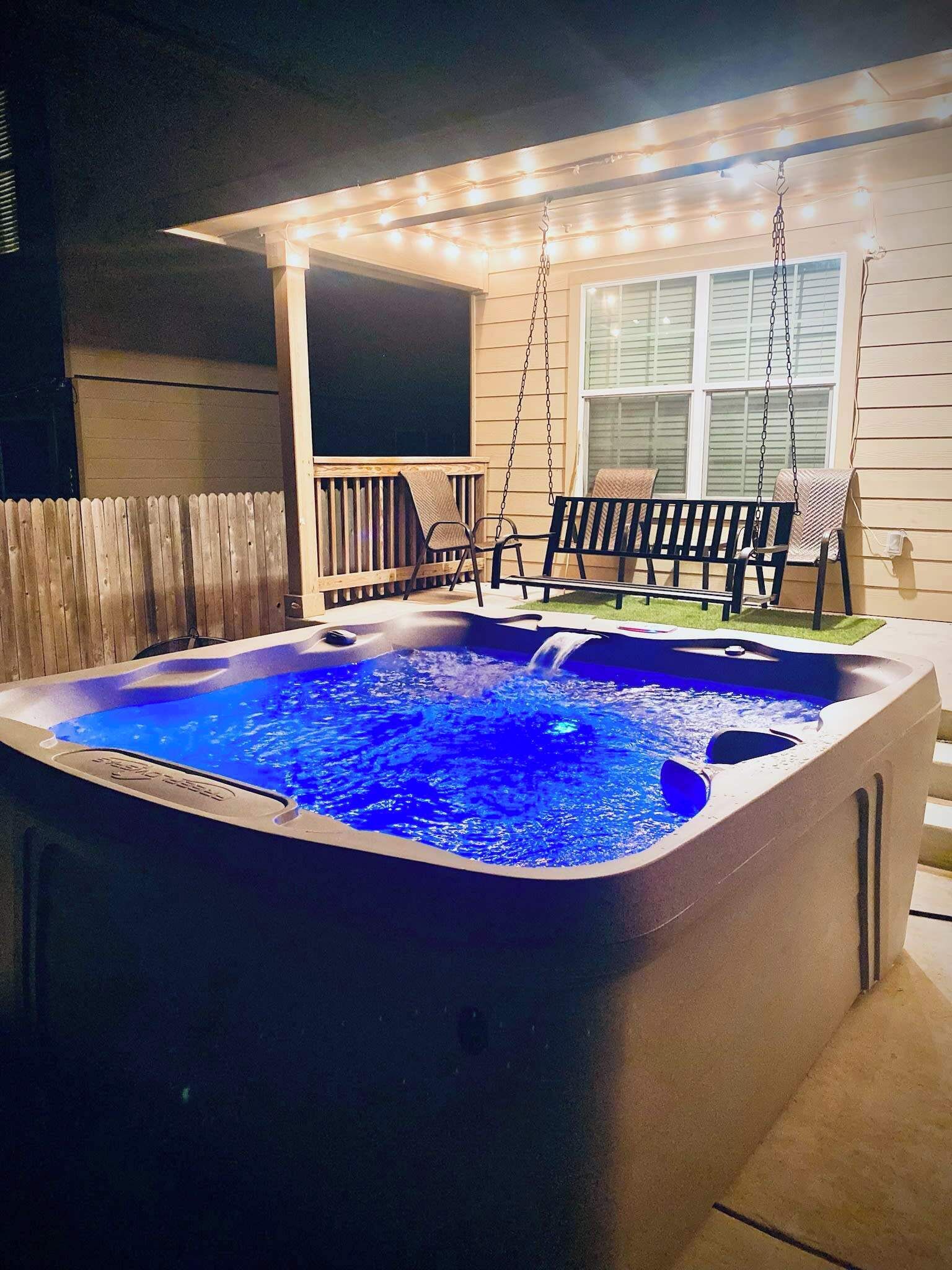 A hot tub with a blue light, a swing set, and a covered patio area.