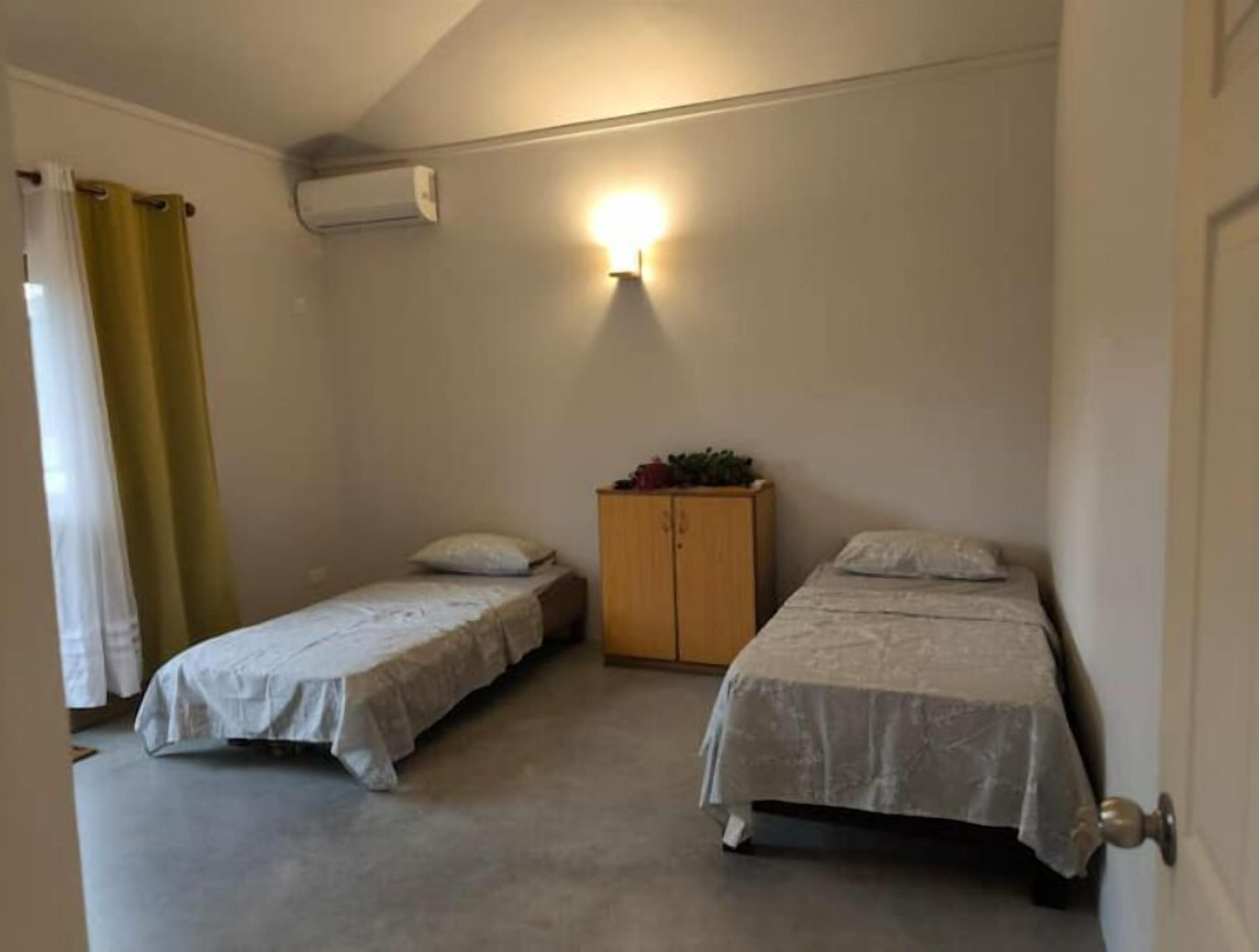 Un petit logement composé d’une seule pièce, comprenant deux lits simples, une armoire en bois et un climatiseur fixé au mur.