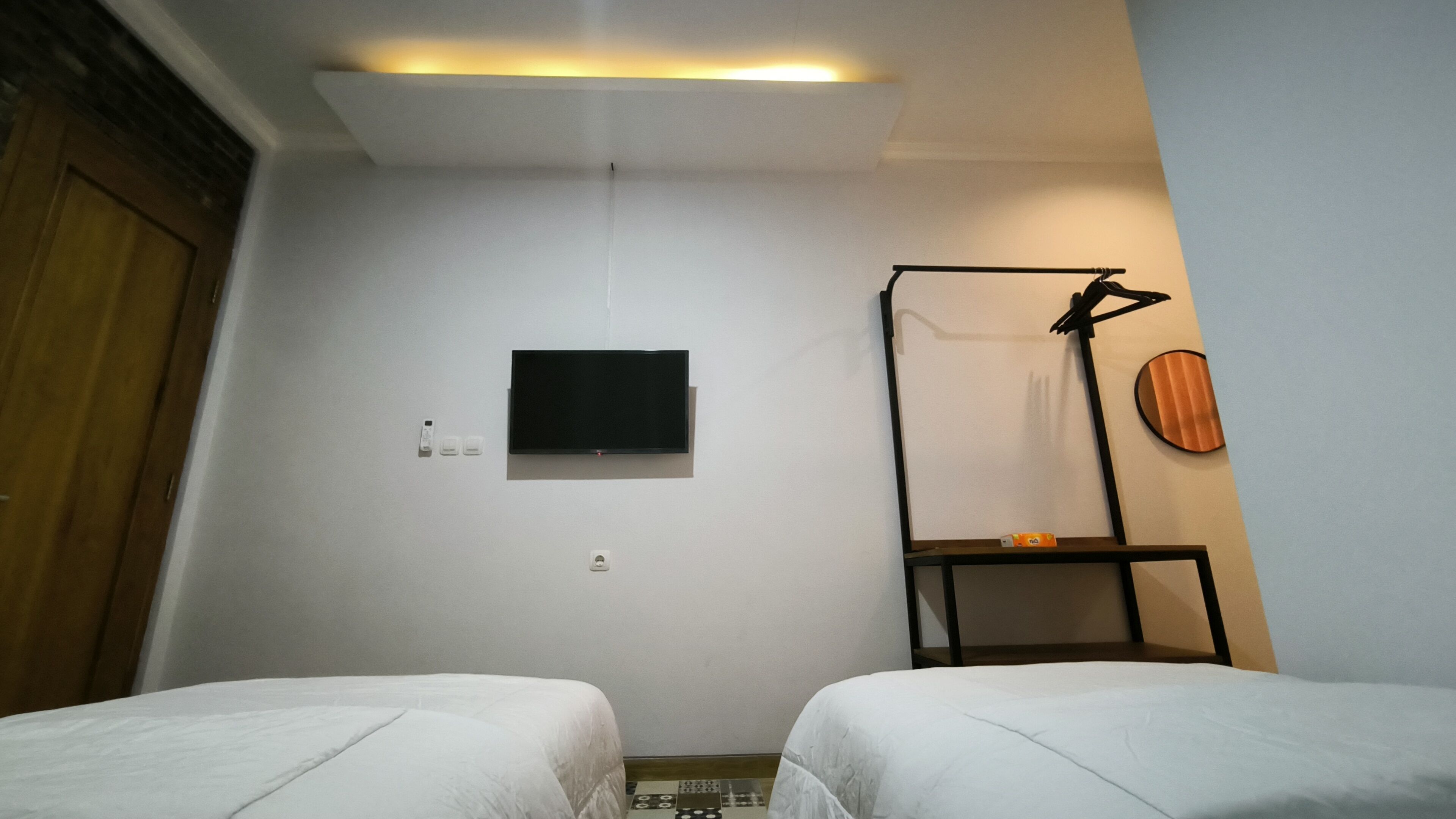 Een kamer met twee bedden, een flatscreen televisie aan de muur, een klein plankje en een deur.
