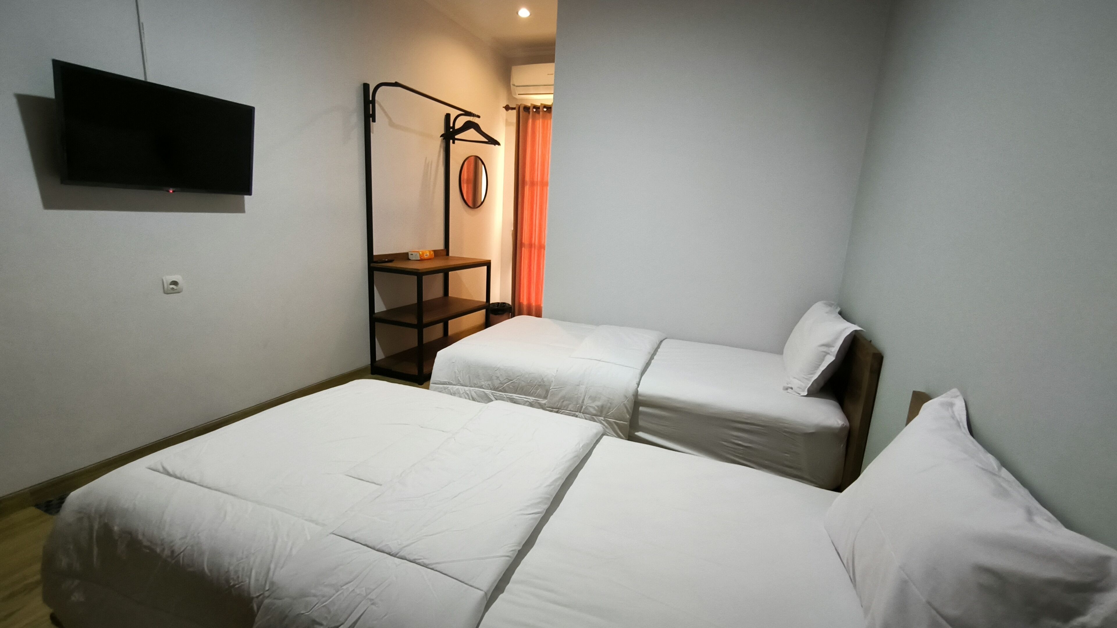 A small, clean room with two single beds, a TV mounted on the wall, and a small table with a mirror.
