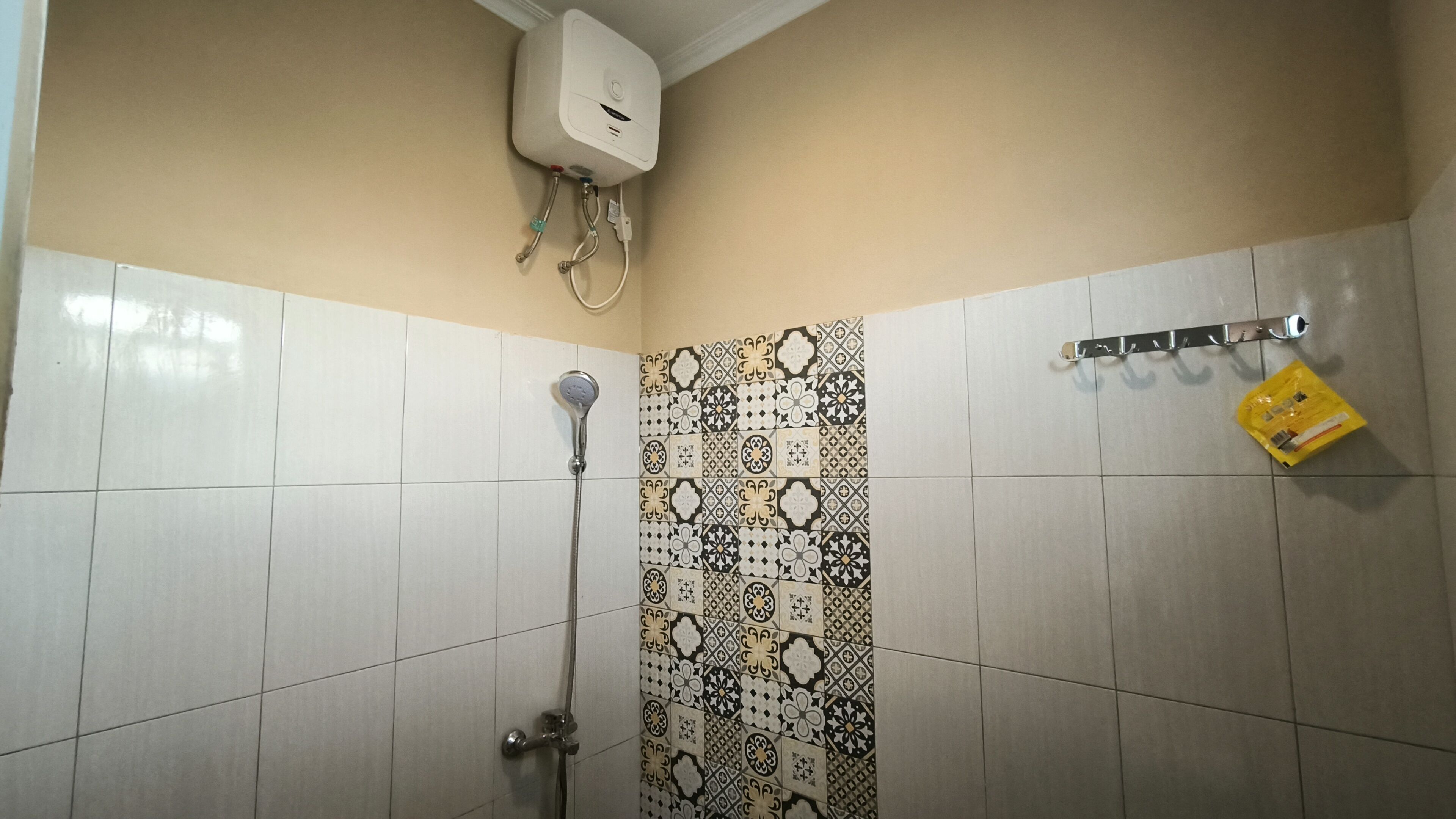 Ein Badezimmer mit weißen Fliesen, einer Dusche, einer Wand mit gemusterten Fliesen und einem gelben Paket auf dem Boden.