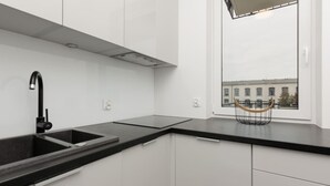 Una cocina moderna con encimera negra, armarios blancos y ventana con vistas a edificios.