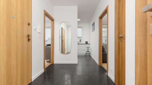 Un pasillo con puertas de madera, un espejo y una zona de cocina al fondo.