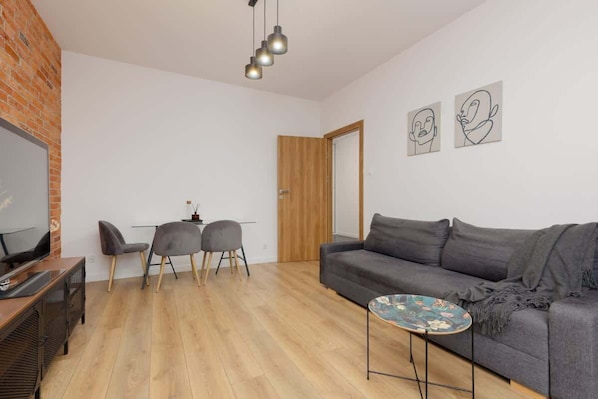 A modern living room with a grey sofa, a TV, a dining table with chairs, and artwork on the wall.