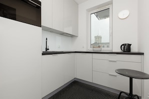 A modern kitchen with white cabinets, a black countertop, a window with a view, a clock, and a kettle.