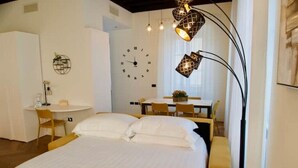 A hotel room with a bed, a desk, a chair, a clock, and a lamp. - Casa Romano Suites eco apartment AMBRA (Trieste)