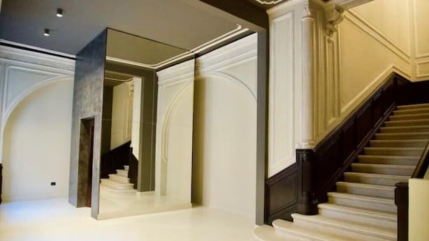 A grand staircase with a dark wooden handrail and white steps, leading to a landing with a large mirror reflecting the room. - Casa Romano Suites eco apartment AMBRA (Trieste)