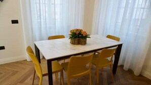 A dining area with a white table and yellow chairs, a woven centerpiece, and a wooden floor. - Casa Romano Suites eco apartment AMBRA (Trieste)