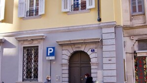 A building with a large arched entrance, a blue parking sign, and a door with a small sign above it. - Casa Romano Suites eco apartment AMBRA (Trieste)