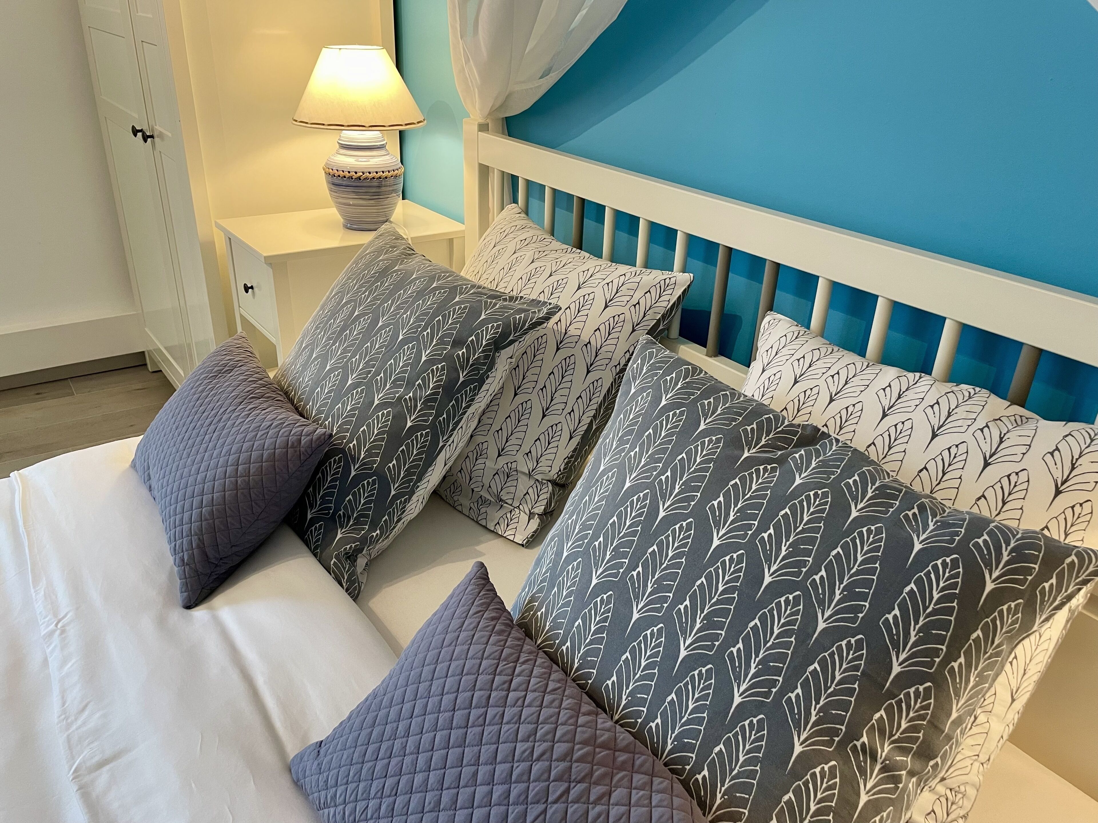 A bedroom with a bed, multiple pillows, a bedside lamp, and a nightstand.