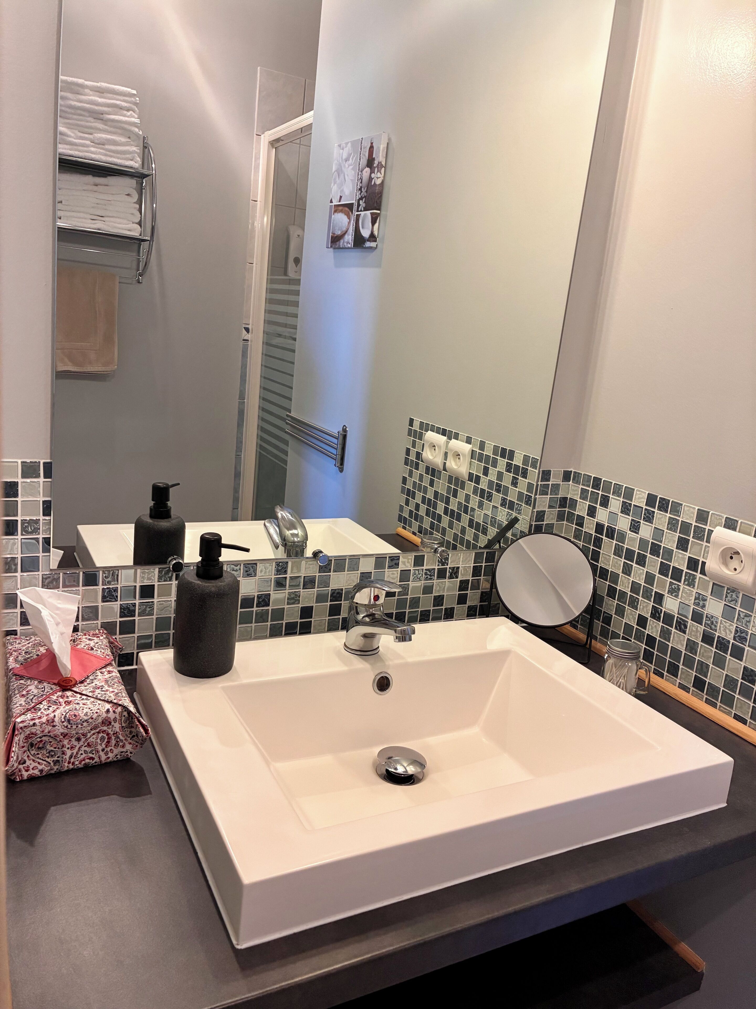 A bathroom with a white sink, a mirror, a towel rack, and a tiled backsplash.