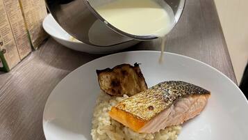 Una persona vertiendo un líquido cremoso en un tazón blanco que contiene arroz y un trozo de pescado.