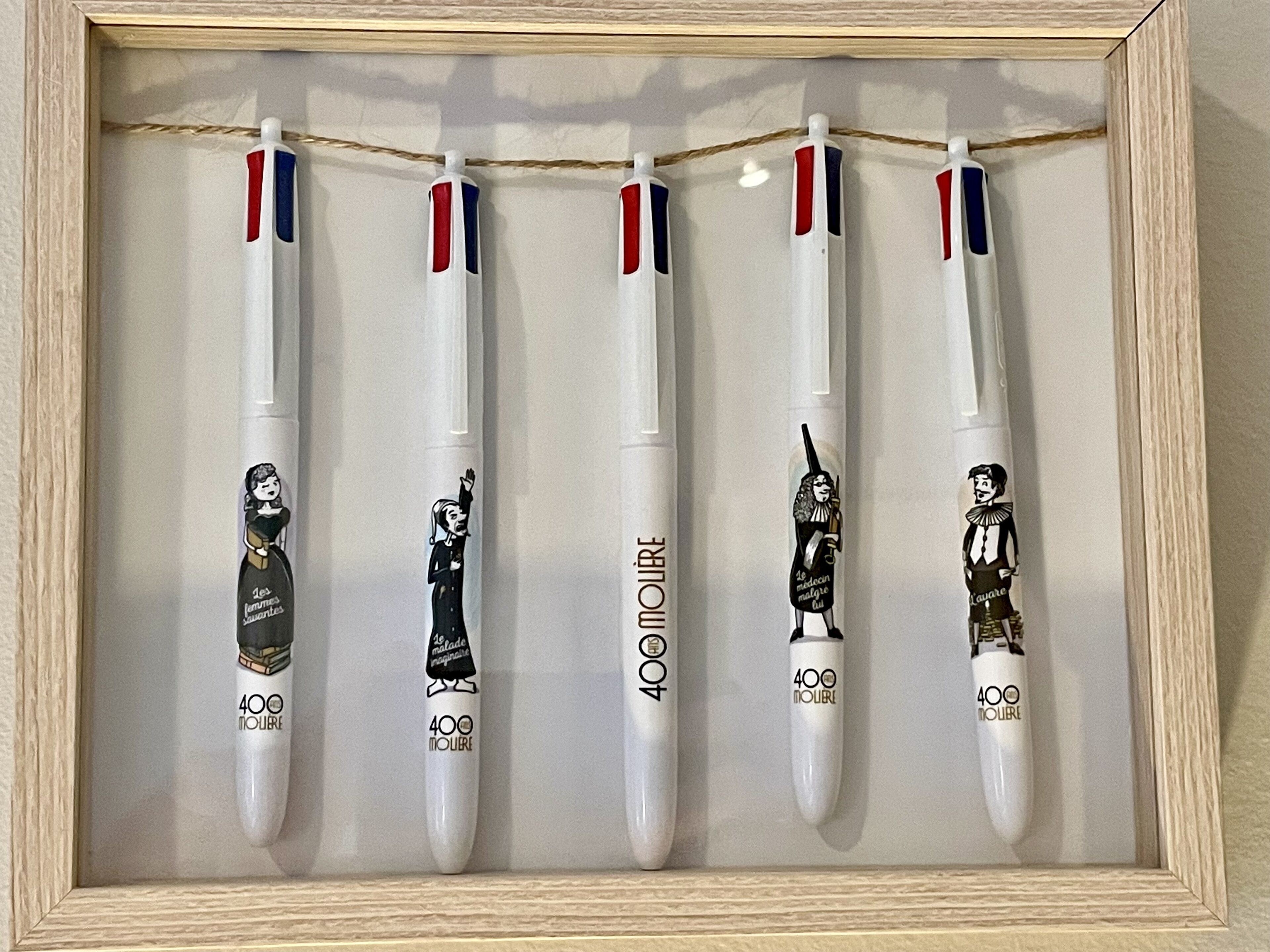 A framed display of five white pens with red, white, and blue stripes, each featuring a different cartoon character and the text "400 MOURE".