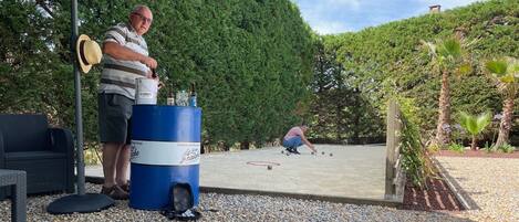 Un espacio al aire libre con un barril azul, un sombrero en un palo, y una persona jugando croquet.