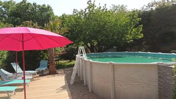 A backyard with a swimming pool, lounge chairs, and a red umbrella.