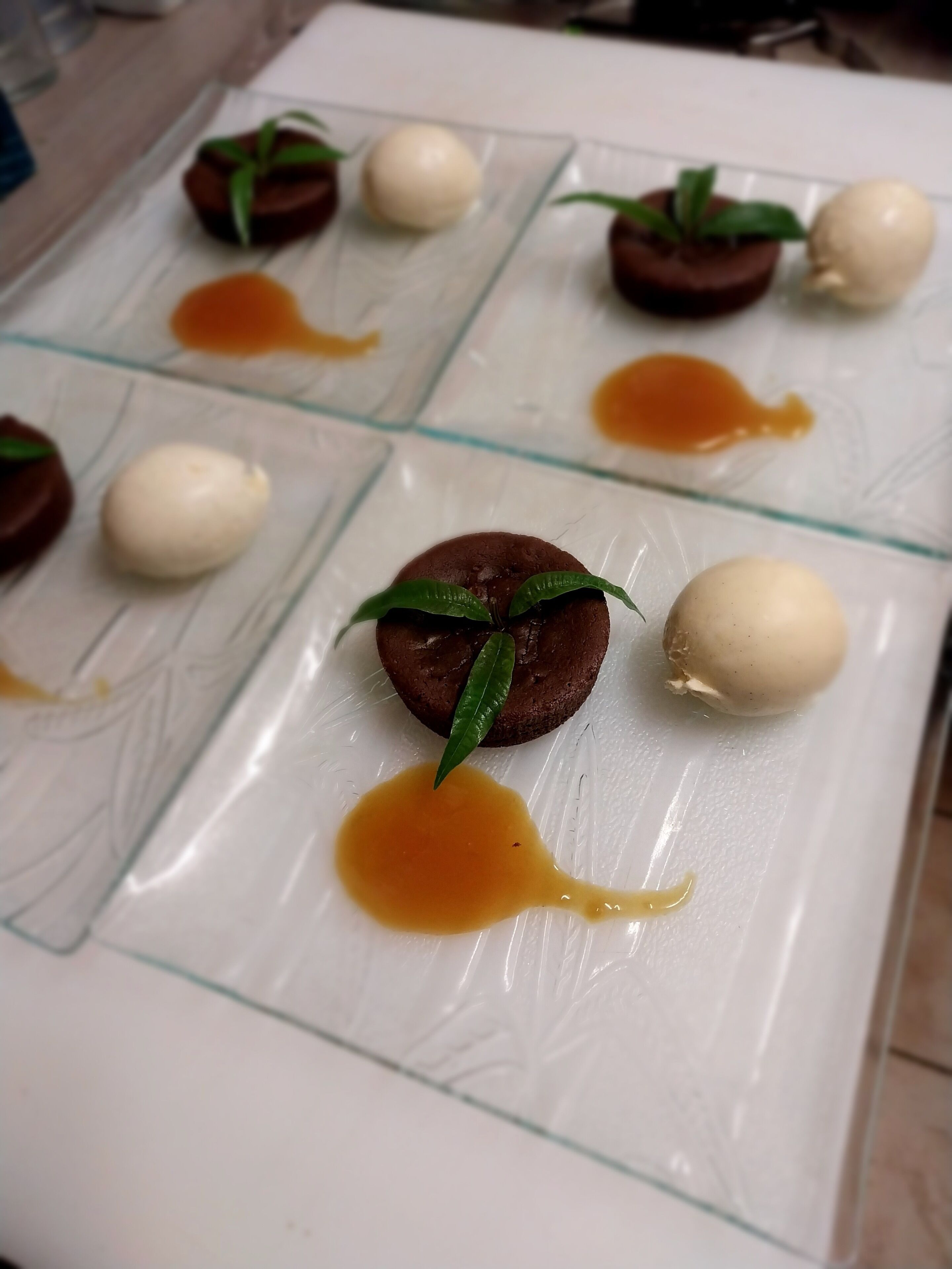 Un plato de postre con bombones de chocolate y blanco, decorado con hojas verdes y cubierto con salsa de caramelo.