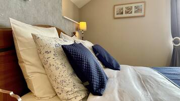 A neatly made bed with floral and quilted pillows, a wooden headboard, a bedside lamp, and a framed picture on the wall.