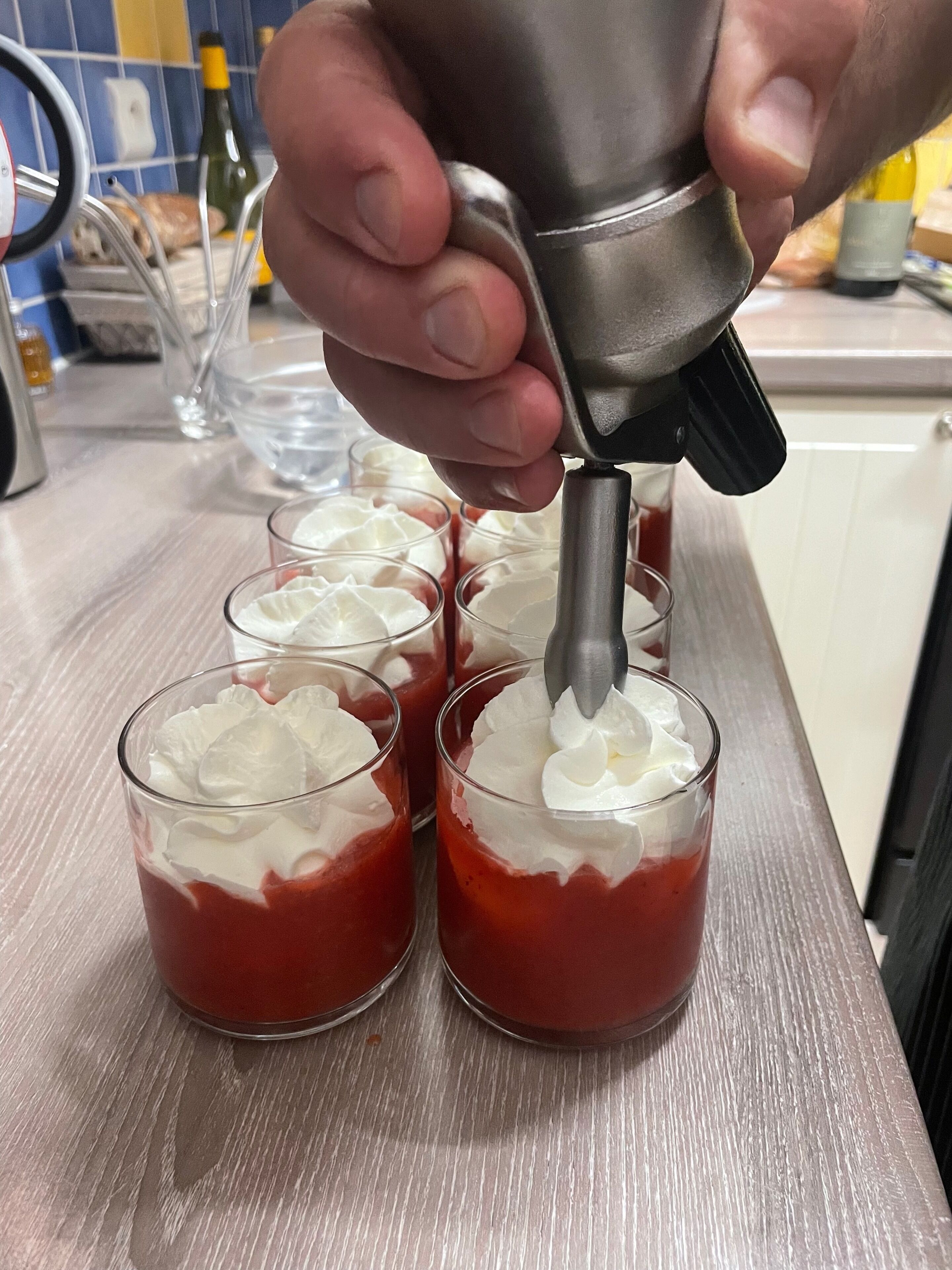 Una persona usando un electrodoméstico de cocina para añadir crema batida a vasos de postre.