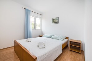 Ein Schlafzimmer mit einem hölzernen Bett, weißer Bettwäsche, einem blauen Vorhang, einem kleinen Nachttisch und einem gerahmten Bild an der Wand.