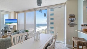 Un comedor con un amplio ventanal con vistas a la playa, un televisor y una pared decorada con motivos náuticos.