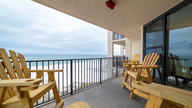 Ein Balkon mit Holzsesseln und -tischen mit Blick auf einen Strand.