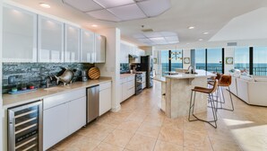 A modern kitchen with white cabinets, a central island, and a view of the ocean. - Phoenix IX 1101 by Liquid Life (Orange Beach)