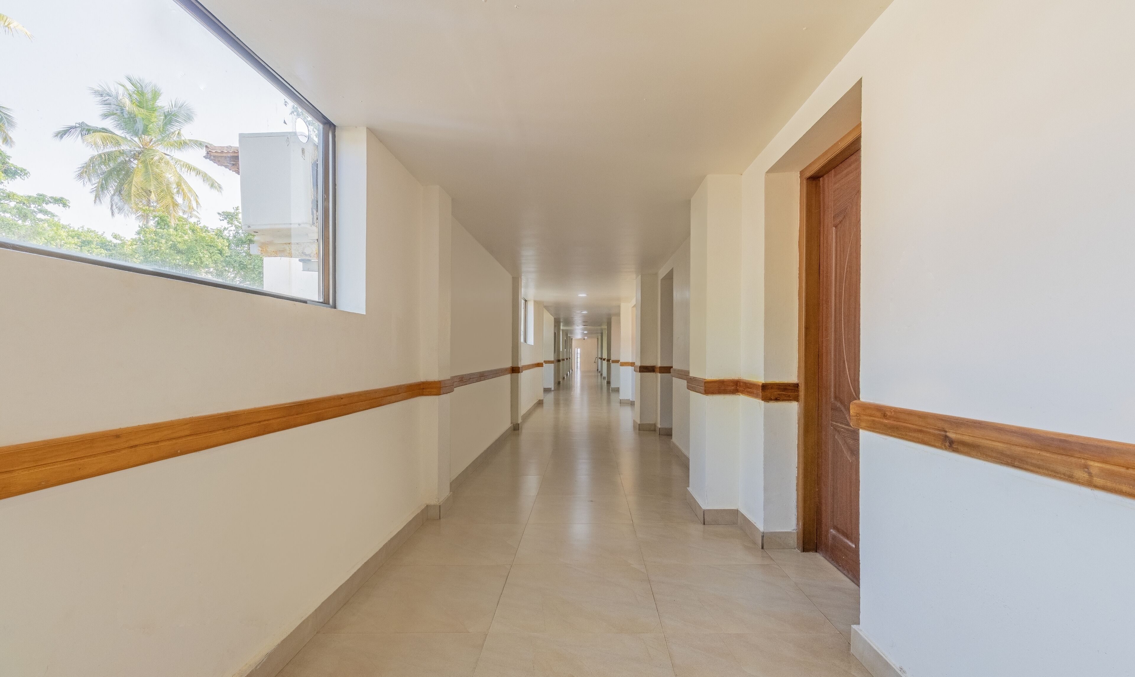 A long, narrow hallway with white walls and wooden trim, leading to a door at the end.