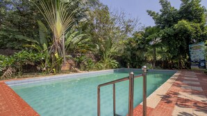 A swimming pool with a tiled edge, surrounded by lush greenery and a brick pathway. - Treebo Sadhoo Heritage (Kannur)