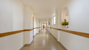 A long, narrow hallway with white walls and wooden trim, leading to a door at the end. - Treebo Sadhoo Heritage (Kannur)