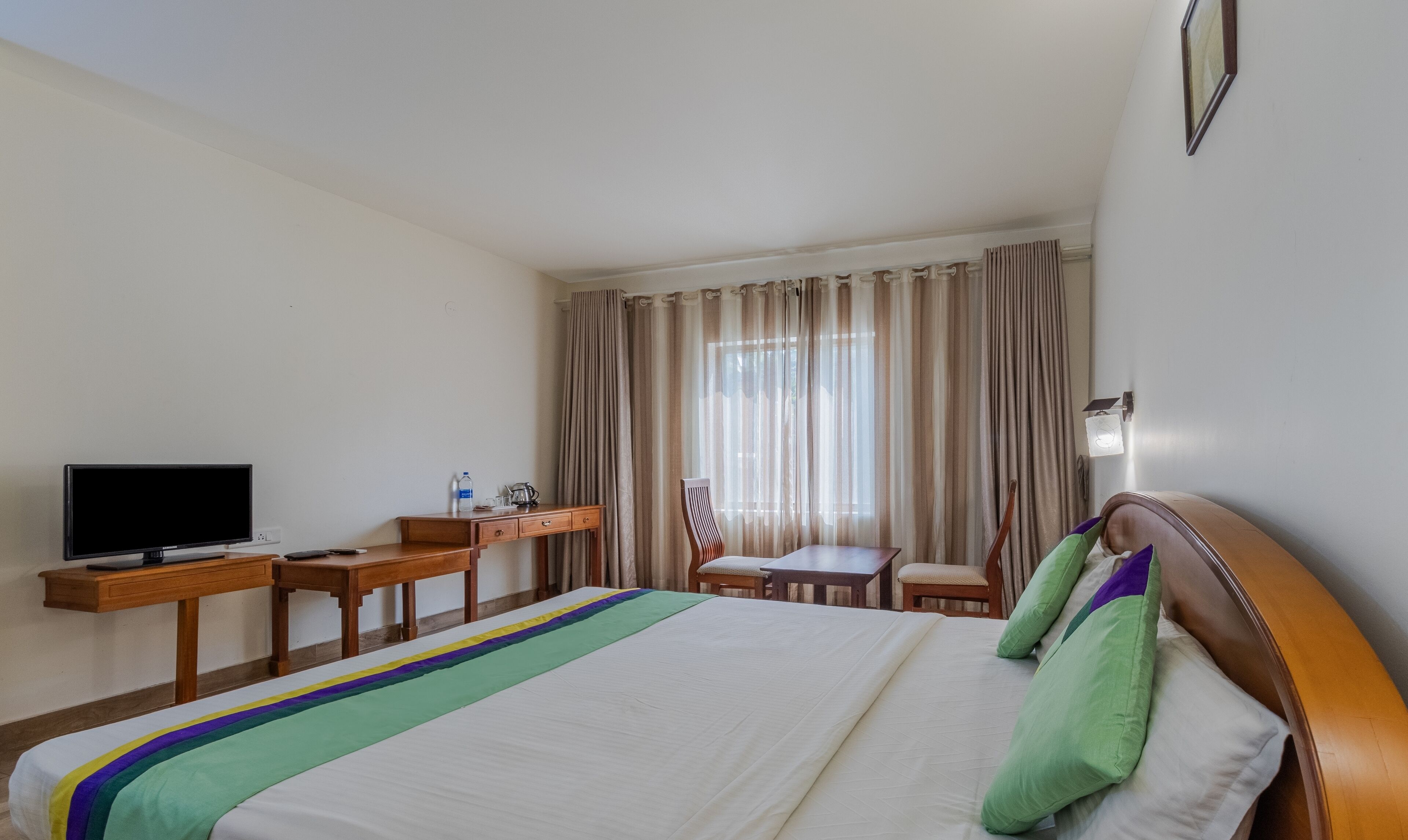 A hotel room with a bed, a desk with a television, a chair, and a window with curtains.