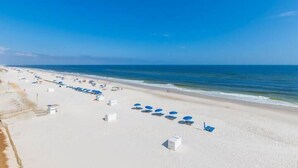 A beach with rows of white beach chairs and umbrellas, a clear blue sky, and the ocean in the background. - Sea Glass 406 by Liquid Life (Gulf Shores)