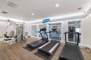 Een sportschool met loopbanden, krachttoestellen en een televisiescherm.