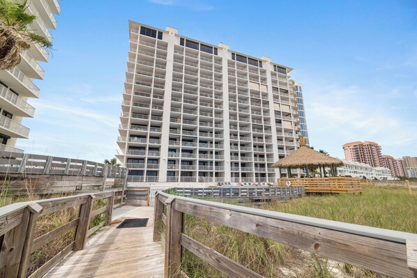 Un hôtel à plusieurs étages doté de balcons, d’une promenade en bois et d’une plage avec une structure recouverte de chaume.
