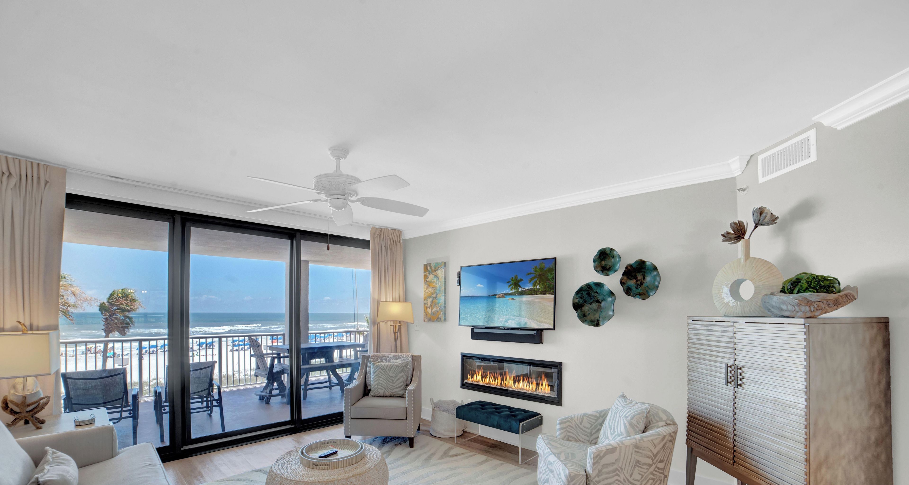 Een moderne woonkamer met een grote schuifpui naar een balkon, een open haard en uitzicht op het strand.