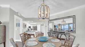 Un comedor con una mesa redonda de madera, individuales blancos y azules estampados, y un cuenco azul como adorno central. Se ven un espejo grande y una lámpara colgante en las paredes.