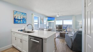 A kitchen with a large island, a dining area with a table and chairs, and a living room with a sofa. - Tradewinds 701 by Liquid Life (Orange Beach)